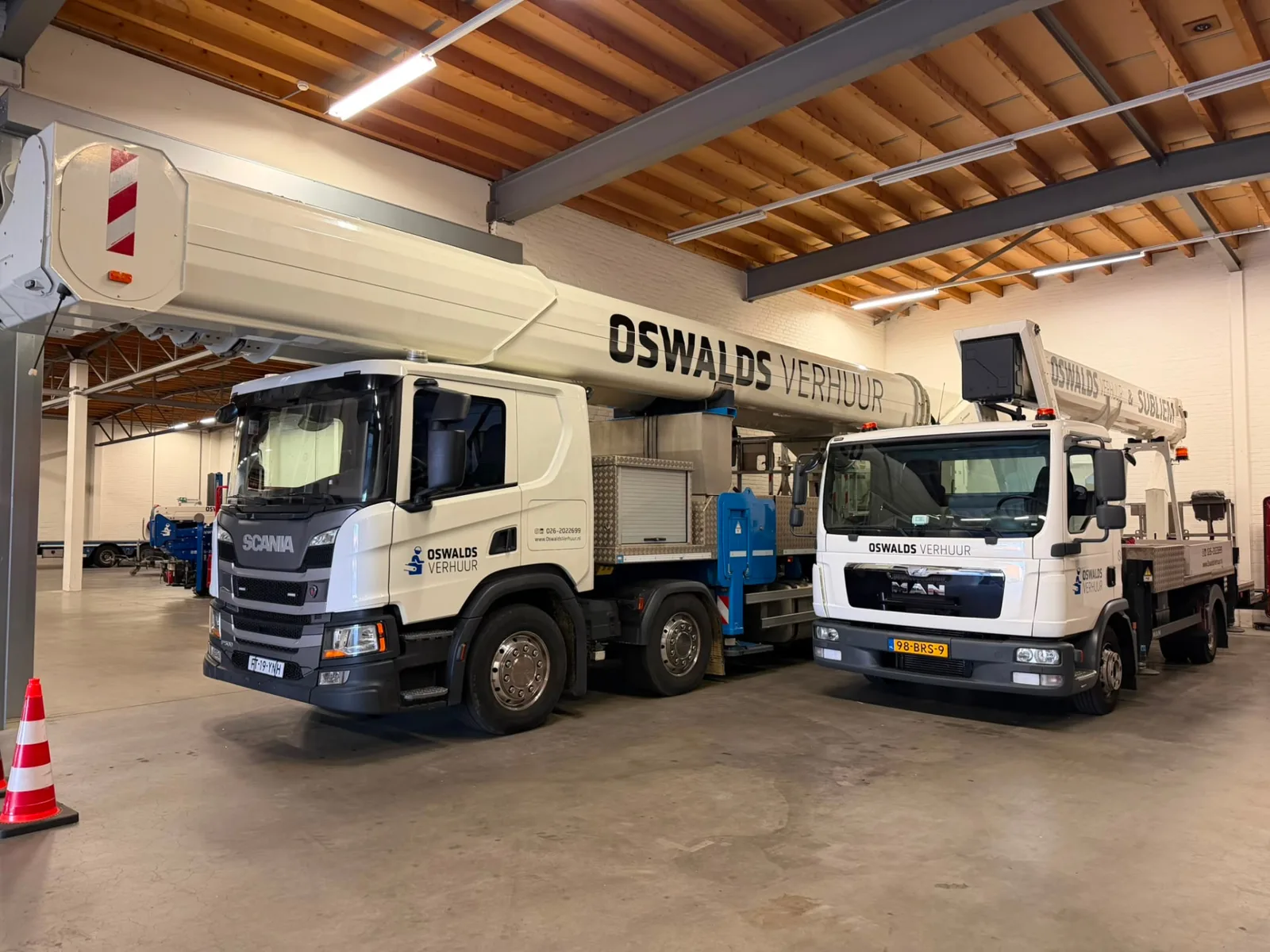 90 meter RUTHMANN T900HF met Oswalds Verhuur belettering naast een kleinere vrachtwagenhoogwerker in de loods in Arnhem